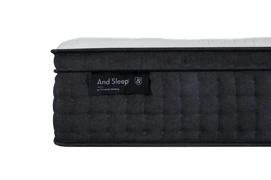 Close-up of a dark quilted mattress with 'And Sleep' label and white top surface.