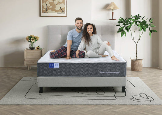 Smiling couple sitting on modern mattress in stylish bedroom with grey bed base
