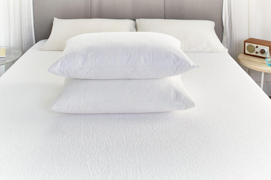 White cotton terry pillows stacked on a bed with a light grey upholstered headboard