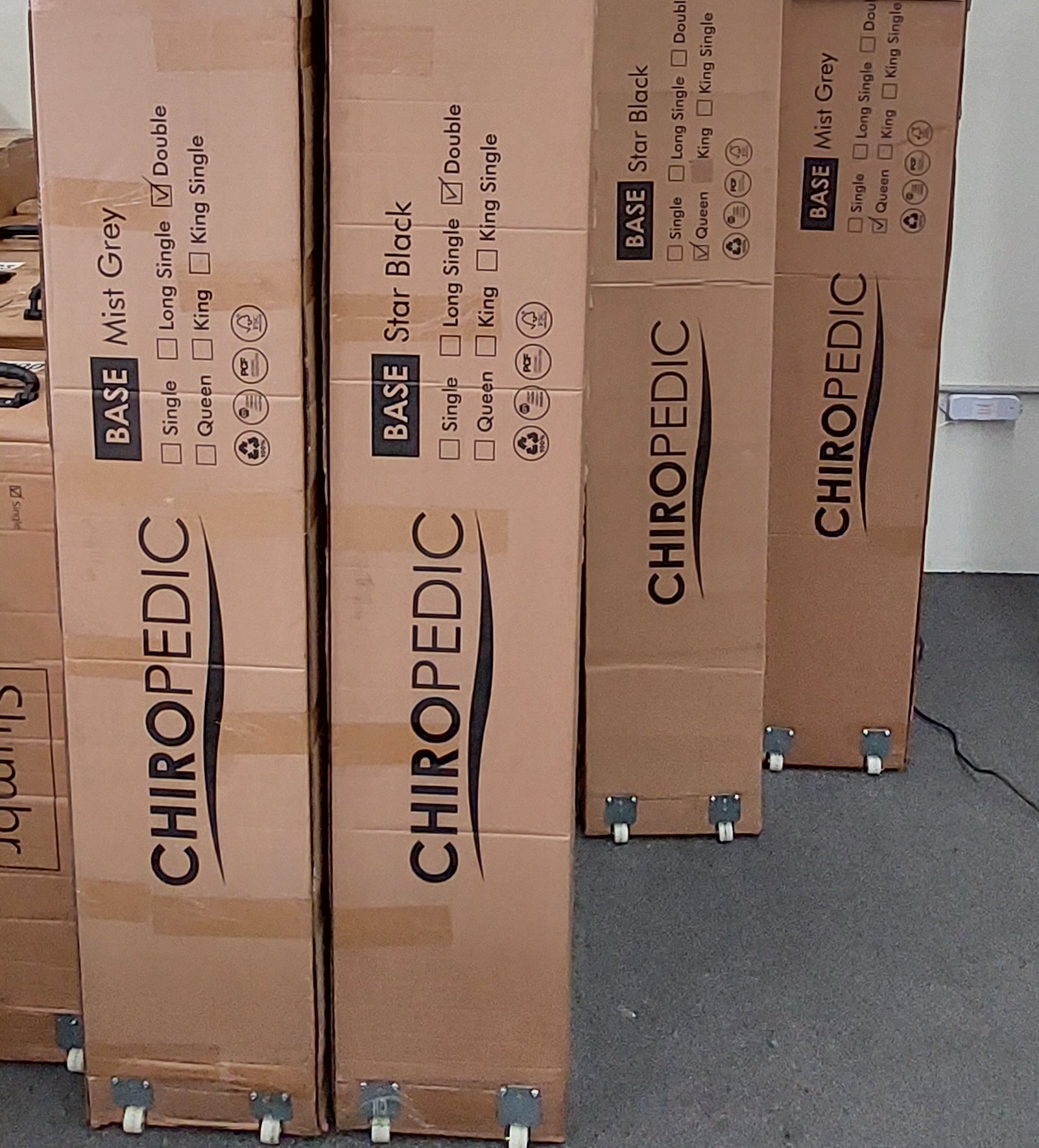 Mattress base boxes labeled Chiropedic in Mist Grey and Star Black on wheels, ready for delivery.