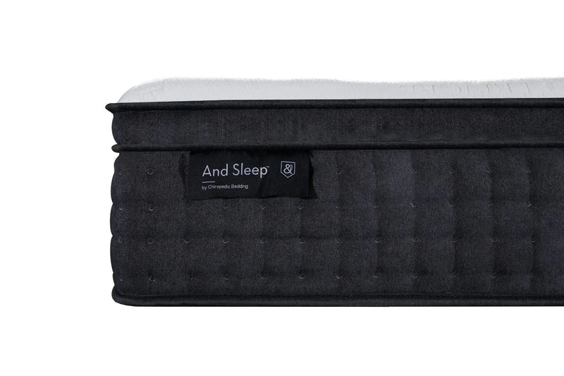 Close-up of a dark quilted mattress with 'And Sleep' label and white top surface.