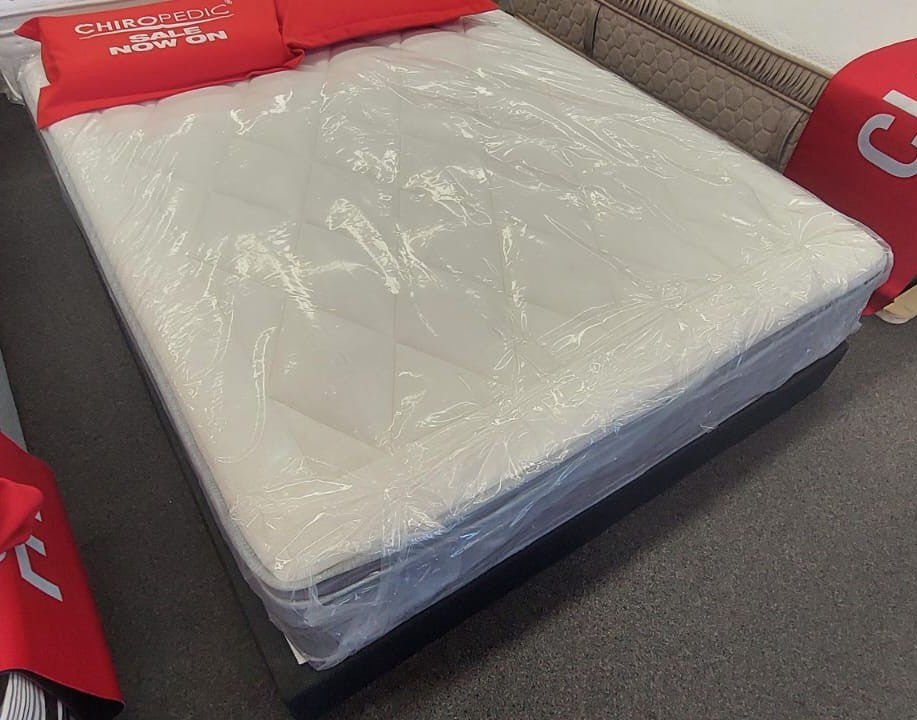 Factory-direct quilted mattress covered in plastic, displayed on a showroom floor