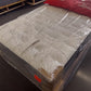 Factory-direct mattress wrapped in plastic, displayed in showroom with red pillows.