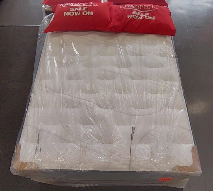 Factory-direct queen mattress wrapped in plastic with red sale pillows on showroom floor